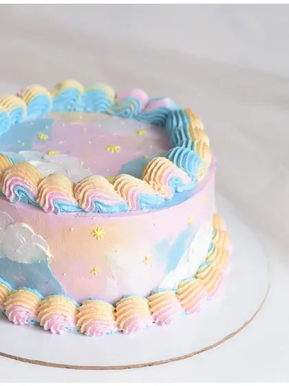 A dreamy pastel galaxy cake. The soft blend of pink, blue, and yellow creates a beautiful watercolor sky effect, complete with tiny stars and clouds.
