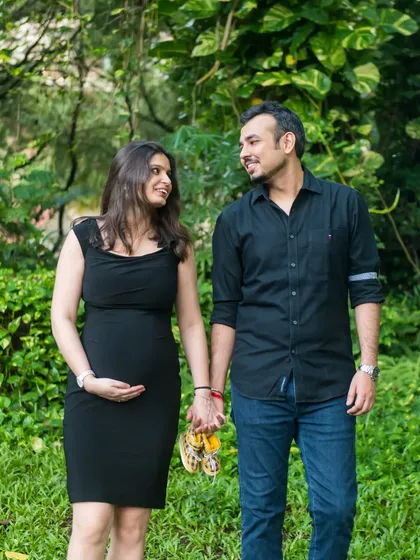 A casual and sweet photo of a couple walking hand-in-hand in the park, holding a pair of baby shoes.