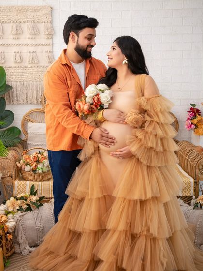 The couple shares a loving gaze, surrounded by the warm, earthy tones of the boho set. The husband's gentle touch on her arm shows his support and affection.