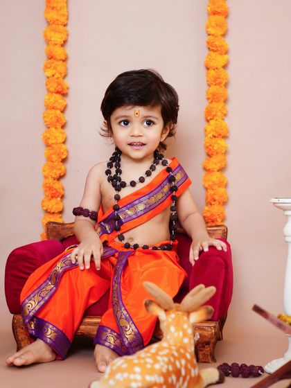 A sweet little boy dressed as Lord Rama, sitting on a miniature throne with a toy deer. A perfect setup for a traditional themed shoot.