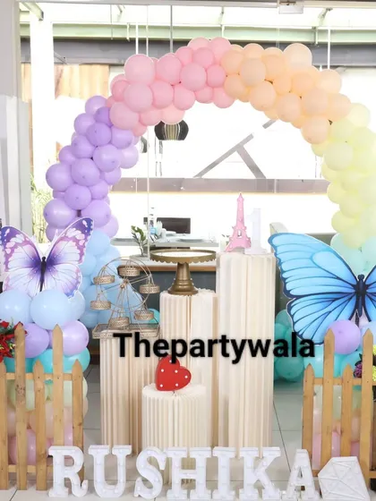 Another view of the pastel rainbow butterfly theme, showing the full arch and the arrangement of pedestals and props. It's a perfect backdrop for cake cutting.
