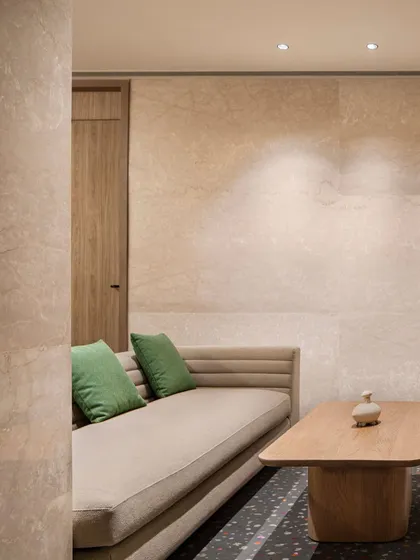 A quiet seating nook on the mezzanine level of the Elevate Clubhouse. The combination of stone-clad walls, a simple sofa, and a wooden coffee table creates a minimalist and calming corner.