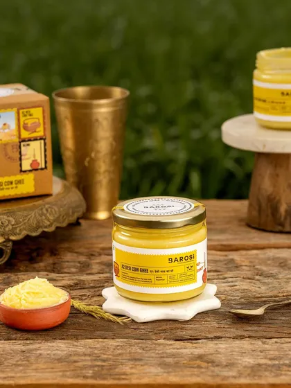 A styled shot of Barosi's cow ghee on a rustic wooden table. The composition with traditional brassware and a small bowl of ghee emphasizes its purity and traditional value.