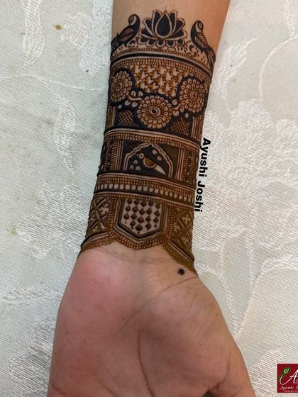 The completed arm band for the engagement mehendi, featuring love birds, a central lotus, and floral patterns.