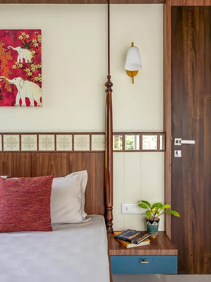A close-up of the bedside in the traditional Indian-themed room, showcasing the beautiful elephant artwork, wooden headboard, and classic wall sconce.
