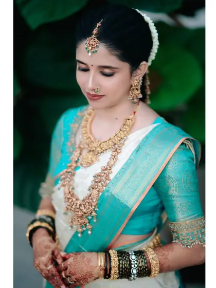 A detailed bridal portrait showcasing the intricate gold jewelry, vibrant silk saree, and delicate henna that are all part of the South Indian bridal look.