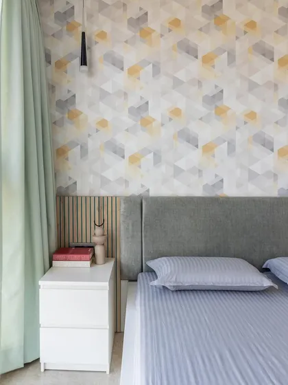 A geometric wallpaper in grey and yellow adds a modern, dynamic touch to this bedroom, balanced by a simple grey headboard and soft mint green curtains.