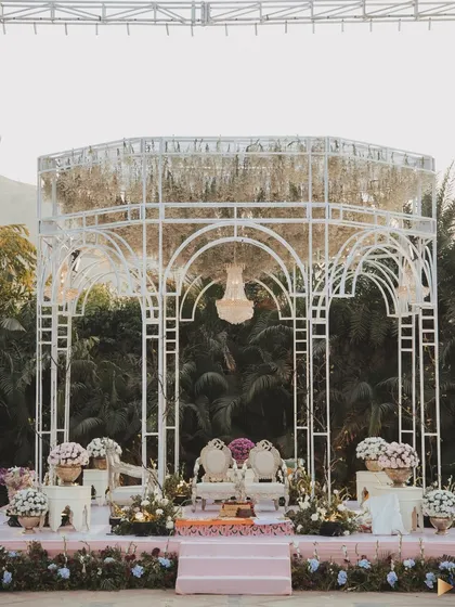 Set against the lush greenery of Udaipur, this elegant white mandap features a delicate, open-air structure with a canopy of hanging white florals and a central chandelier, creating a light and airy feel.