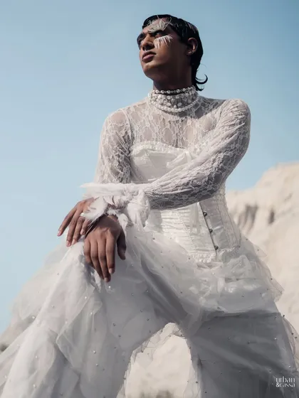 A seated pose showing the full styling of the 'White Feathers' look, with the feather eye makeup complementing the all-white lace and tulle outfit.