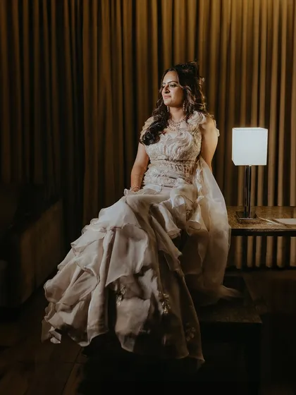 An elegant portrait of the bride seated on a table, her beautiful gown cascading down, captured in a softly lit room.