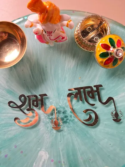 This shot focuses on the traditional elements of the pooja thali, including the "Shubh Labh" text, a Ganesha idol, and holders for kumkum and a diya.