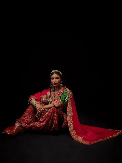 A full-length seated portrait for Debyani & Co against a stark black background, emphasizing the vibrant colors of the outfit.