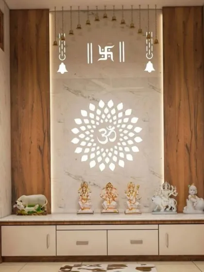 A modern pooja unit defined by its clean lines and powerful symbolism. The design features a large, backlit Om mandala on a white marble-finish backdrop, flanked by wood panels. Hanging bells and Swastik symbols add traditional touches to this elegant space.