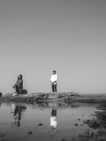 A wider perspective of the couple by the water, emphasizing the vastness of the landscape. This minimalist black and white composition creates a feeling of peaceful solitude.