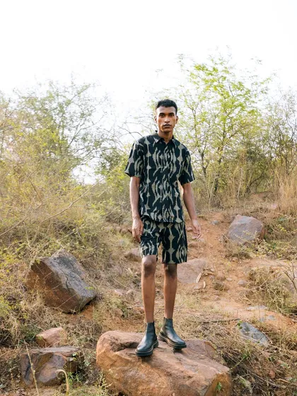 A full-length shot from the "Nazaar" editorial. The model stands on a rock in a rugged, natural landscape, showcasing a modern printed co-ord set.