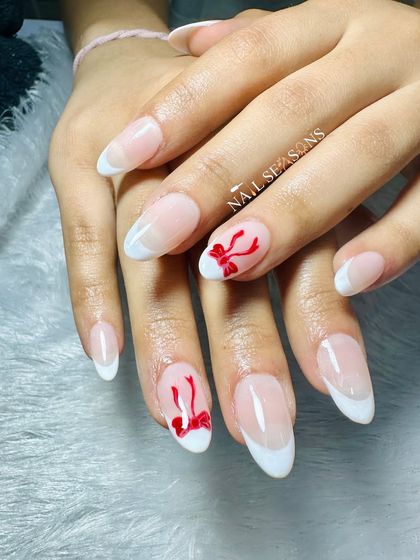 An elegant French manicure with a cute, hand-painted red bow accent.