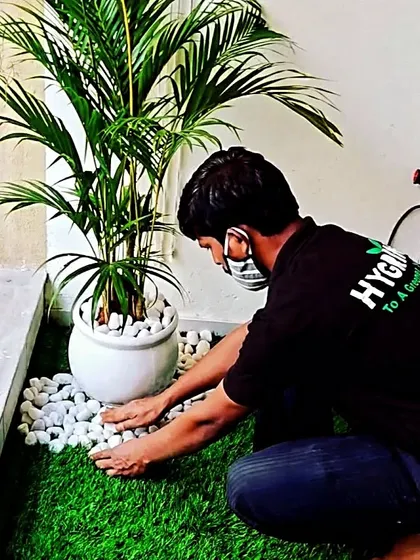 Even a small balcony can become a green escape. Here, my team member is carefully arranging white pebbles around a potted palm on artificial grass, demonstrating the attention to detail I bring to every balcony garden project.