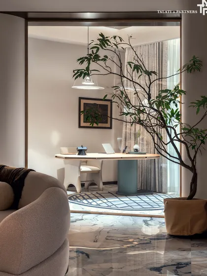 A close-up of a study nook within the living room of the Palais Royale apartment. The design embraces quiet luxury, with a minimalist desk and chair framed by a large potted tree, creating a serene workspace with a magnificent view.
