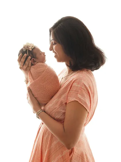 A mother gazes at her newborn, held securely in her arms. The bright, clean background makes this a timeless and classic portrait.
