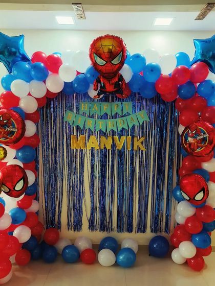 A classic Spider-Man theme for a home birthday party. The decoration includes a blue tinsel curtain, a balloon arch in red, white, and blue, and multiple Spider-Man foil balloons.