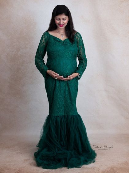 A full-length view of our gorgeous emerald green lace gown. This classic standing pose is perfect for showcasing both the dress and the beautiful baby bump.