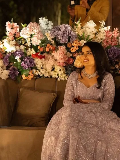 The bride seated amidst a backdrop of beautiful flowers. Her lavender lehenga and soft makeup create a dreamy, romantic look for her Sangeet.