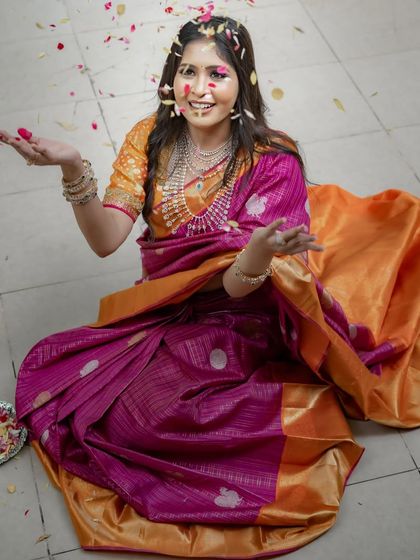 A playful and joyous shot, with flower petals raining down on the model in her bright pink and orange Kancheevaram silk saree.