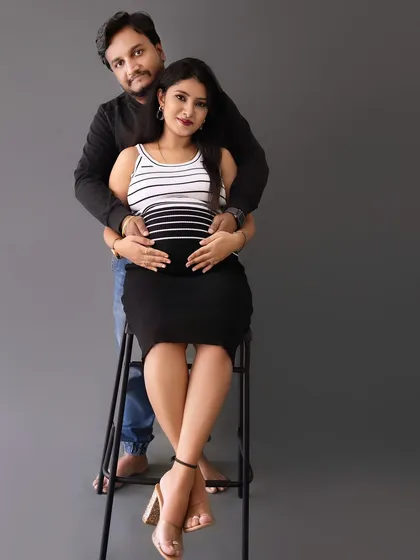 A modern and chic couple's portrait with the mom-to-be seated on a stool, dressed in a striped top and skirt.