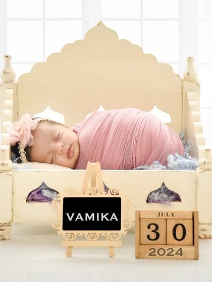 A baby girl sleeps in an ornate, palace-style miniature bed against a bright, clean background. This elegant prop adds a touch of royalty to the newborn session.