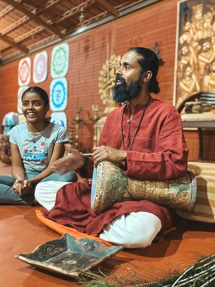 Music is a form of yoga, a path to the divine. Here, I share the joy of drumming with a young visitor, her smile reflecting the universal language of rhythm and song.