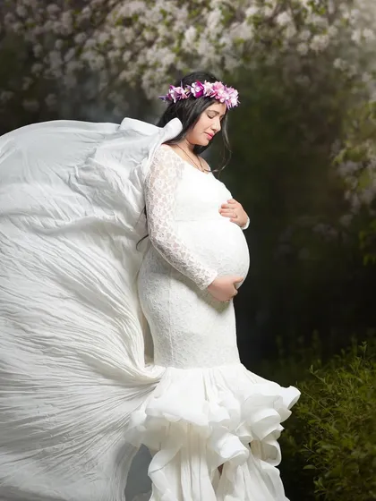 An angelic portrait of a mom-to-be in a white lace gown with a dramatic flowing train. The soft, natural setting and floral crown complete this ethereal maternity look.
