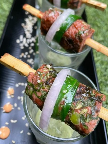 Juicy mutton seekh kebabs on a skewer, wrapped with onion and capsicum and served in a shot glass with green chutney. A classic starter presented with modern flair.
