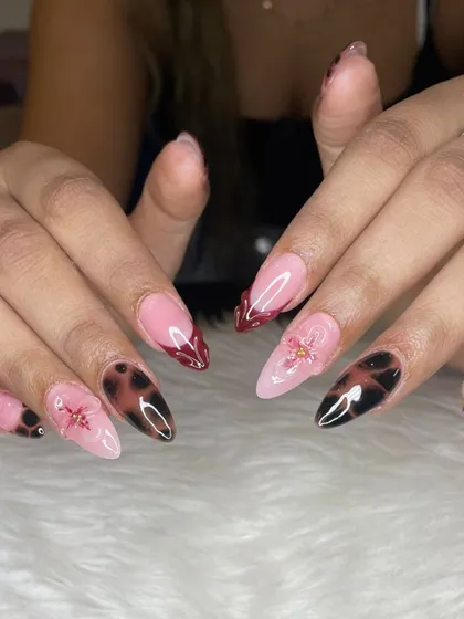 For when you're feeling moody and glam. This set features a mix of trendy tortoise shell nail art, deep red French tips, and delicate 3D floral accents on sharp stiletto extensions.