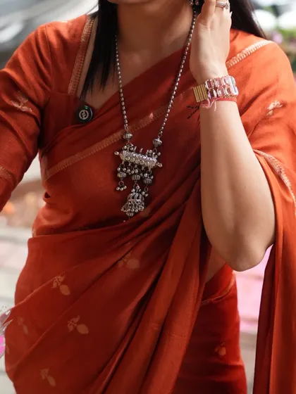 A detailed shot of the rust orange saree styled with a silver tribal necklace, showing its versatility.