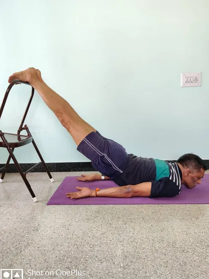 Viparita Shalabhasana (Inverted Locust Pose) with feet on a chair. This is a powerful back-strengthening pose that prepares the body for arm balances and deeper backbends.
