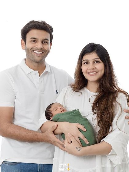 A classic first family portrait, with both parents smiling brightly as they hold their new baby.