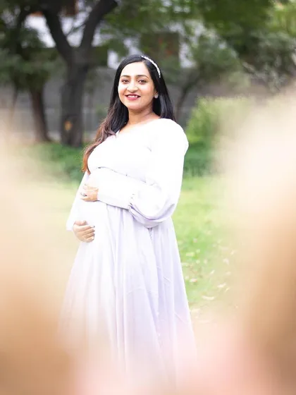 This is a creative and heartfelt shot, framed by the father-to-be's hands making a heart shape. It beautifully centers the expecting mother and her bump, symbolizing that she is the heart of their growing family.