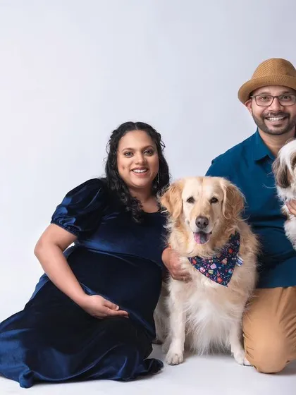 A happy family portrait featuring the expecting couple and their two dogs, a golden retriever and a shih tzu. This studio shot captures the joy and excitement of the entire family, including the furry members, as they await their new arrival.
