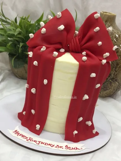 A stylish and elegant cake designed to look like a gift box. This single-tier cake is covered in white ganache and wrapped with a beautiful, hand-sculpted red bow with white floral embossing.