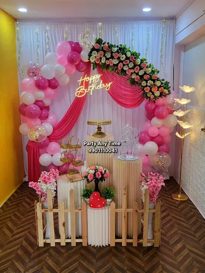 A beautiful pink and white birthday theme perfect for any age. This decoration includes a balloon arch, draped fabric, a floral arrangement over the top, and a "Happy Birthday" neon sign.