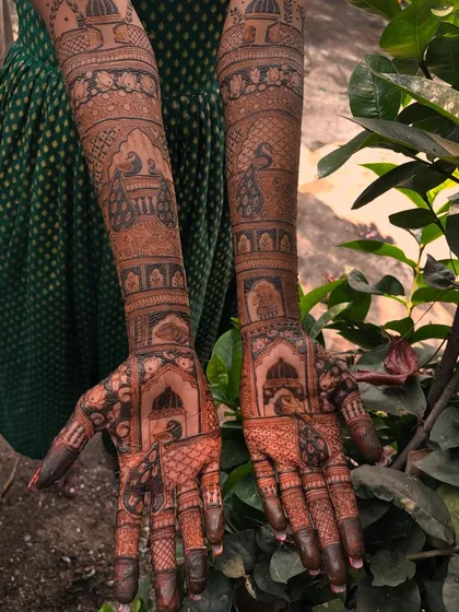 A beautiful shot of a bridal mehendi in a natural setting. The design features peacocks and palace architecture, creating a timeless and elegant look.