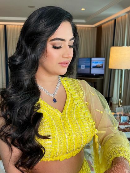 A bride in a bright yellow lehenga, her long, dark hair styled in classic, voluminous waves.