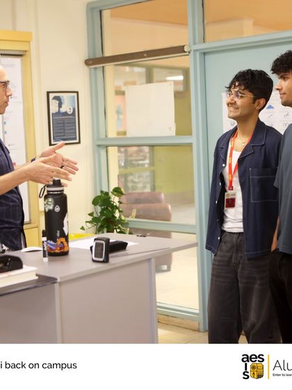 A teacher gestures while speaking with two alumni in a classroom. These interactions show the lasting mentorship and guidance our faculty provide.