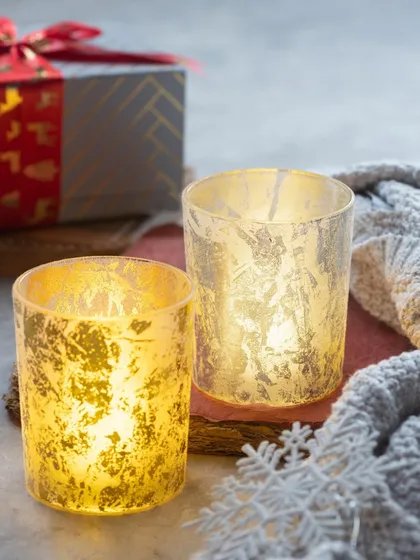 A set of two beautiful gold and silver foil glasses with tea lights. They create a warm, shimmering glow.
