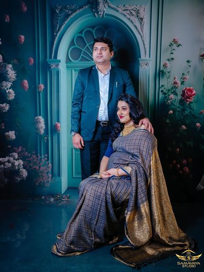 A formal portrait of the couple in a traditional studio setting. His hand on her shoulder signifies support and partnership on this sacred journey.