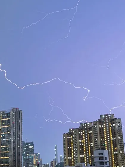 Multiple streaks of lightning spiderweb across the sky above Mumbai's illuminated skyscrapers.
