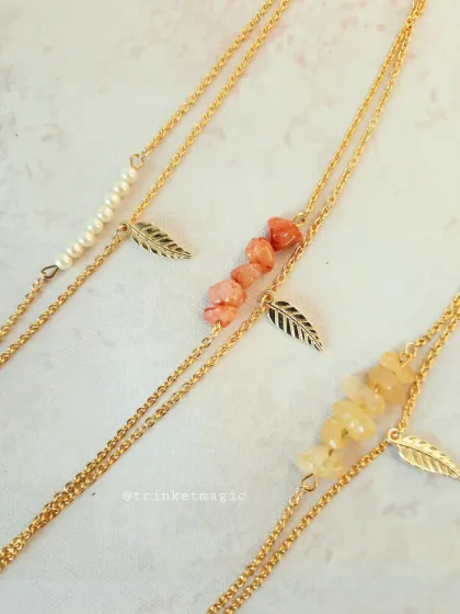 A close-up of the layered pearl and stone bracelets. The delicate golden chains and leaf charms add a touch of nature-inspired elegance.