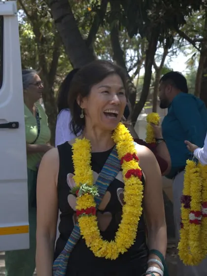 The joyous smile of a guest from our USA and France group, adorned with a traditional welcome garland. Her expression captures the excitement and warmth of arriving at our healing sanctuary.