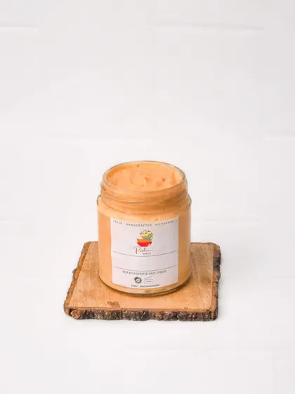 A jar of creamy orange-colored dip, like a chipotle or peri-peri mayonnaise, shot cleanly for a product catalog. The simple setup highlights the product's color and texture.