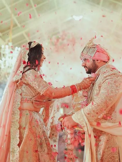 The couple exchanges garlands during the jaimala ceremony, surrounded by a shower of petals and a grand floral decor.
